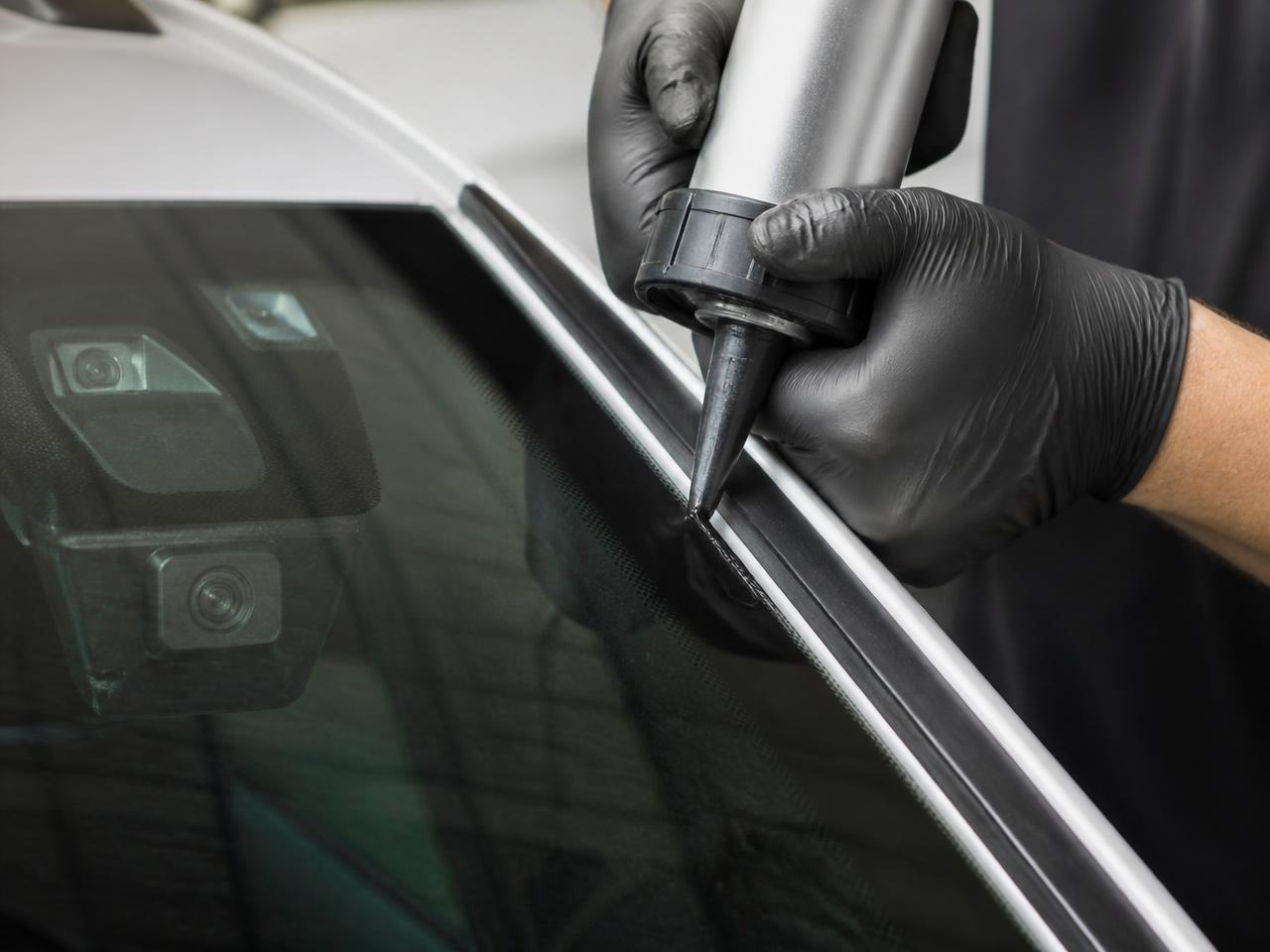 Close-up of urethane being applied along a windshield frame with the ADAS camera bracket visible